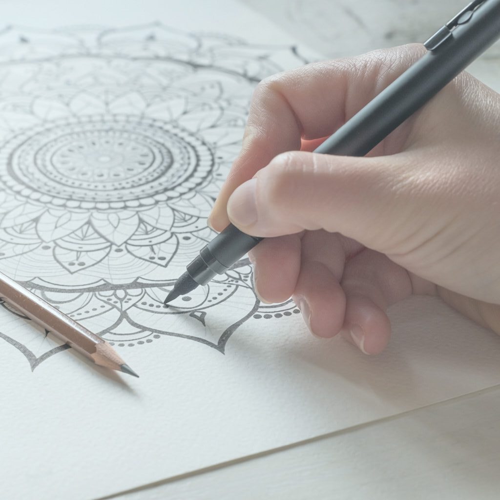Close-up of a hand drawing an intricate mandala with a fine black pen.